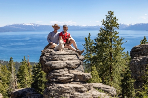 A person and person sitting on a rock with a body of water in the background Description automatically generated with medium confidence